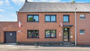A two-story brick building with a tiled roof, a black front door, and windows with flower boxes. - Oasis by Loftigo - Cozy Apartment with Rain Shower (Selfkant)