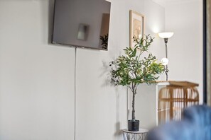 Ein Zimmer mit einem Blumentopf, einem gerahmten Bild, einer Lampe und einem Fernseher an der Wand.