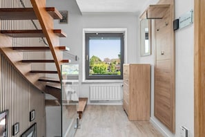 Ein modernes Interieur mit einer Holztreppe, einem Fenster mit Blick auf Grünflächen und einem Holzschrank.