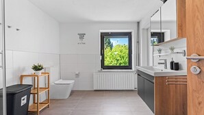 A modern bathroom with a window, a toilet, a sink, and a mirror. - Oasis by Loftigo - Cozy Apartment with Rain Shower (Selfkant)