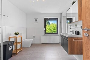 Een moderne badkamer met raam, toilet, wastafel en spiegel.
