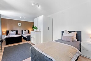 Een moderne slaapkamer met twee bedden, een garderobe, een nachtkastje en een kleine plant.
