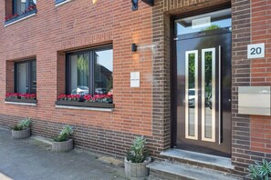 A brick building with a black door, windows with flower boxes, and a number '20' sign. - Forest by Loftigo - Patio & Sunroom (Selfkant)