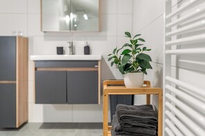 A modern bathroom with a wooden chair, a potted plant, and a towel rack.
