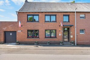 Een gebouw van baksteen met twee verdiepingen, een pannendak, een zwarte voordeur en ramen met bloembakken.