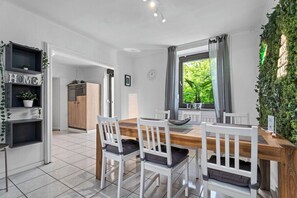 Een moderne keuken met een houten tafel en witte stoelen, een inbouwplank met planten en uitzicht op groen buiten.