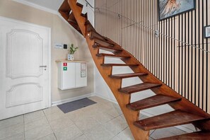 A wooden staircase in a hallway with a white door and a wall-mounted cabinet with emergency instructions.