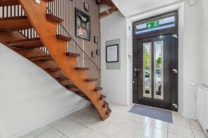 A wooden staircase leading to a dark door with a green emergency exit sign above it. - Forest by Loftigo - Patio & Sunroom (Selfkant)