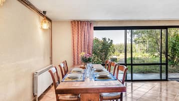 Een eetruimte met een tafel voor vier personen, stoelen, een radiator en uitzicht op een tuin door een glazen deur.