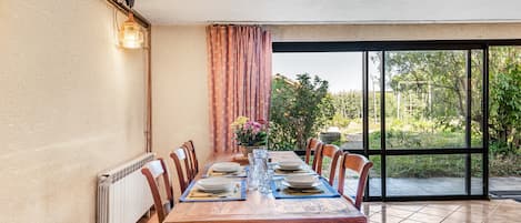 A dining area with a table set for four, chairs, a radiator, and a view through a glass door to an outdoor garden.