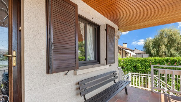 Un banc en bois sur une terrasse carrelée, avec une maison en arrière-plan.