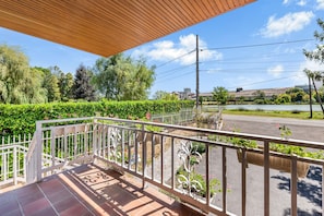 A covered outdoor area with a tiled floor, a white metal railing, and a view of a road and greenery. - Chez Daniel et Zdenka – Cendrine Room (Villars-les-Dombes)