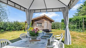 Un espace de restauration en plein air avec une table dressée pour quatre personnes, un bâtiment en bois en arrière-plan et un coin salon abrité.