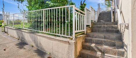 A set of stone steps leading up to a building with a white metal fence and greenery in the background.