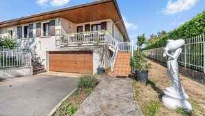Une maison à deux étages avec une façade en bois, un balcon agrémenté de plantes en pot et un garage.