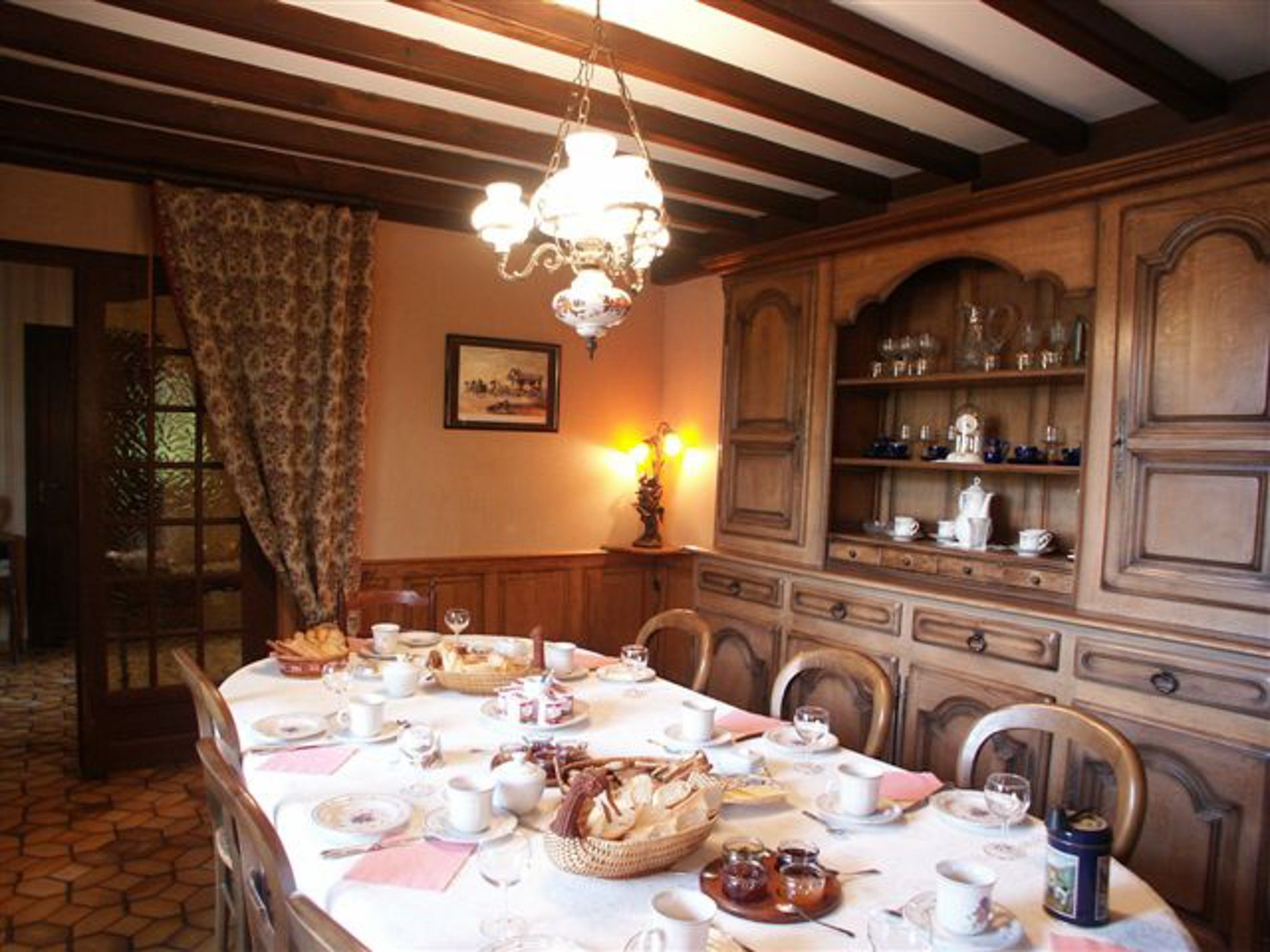 Une salle à manger avec une longue table dressée pour le repas, des meubles en bois et un lustre.