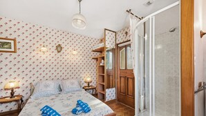 Une chambre à coucher comprenant un lit, deux lampes de chevet, une table de chevet, une armoire en bois, un miroir et un espace douche.