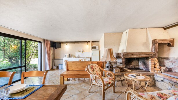 Un salon chaleureux avec une table en bois, des chaises, une cheminée et une cuisine en arrière-plan.