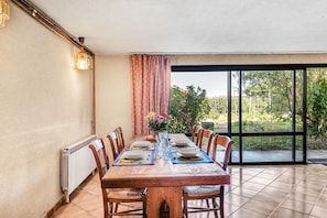 Een eetruimte met een tafel voor vier personen, stoelen, een radiator en uitzicht op een tuin door een glazen deur.
