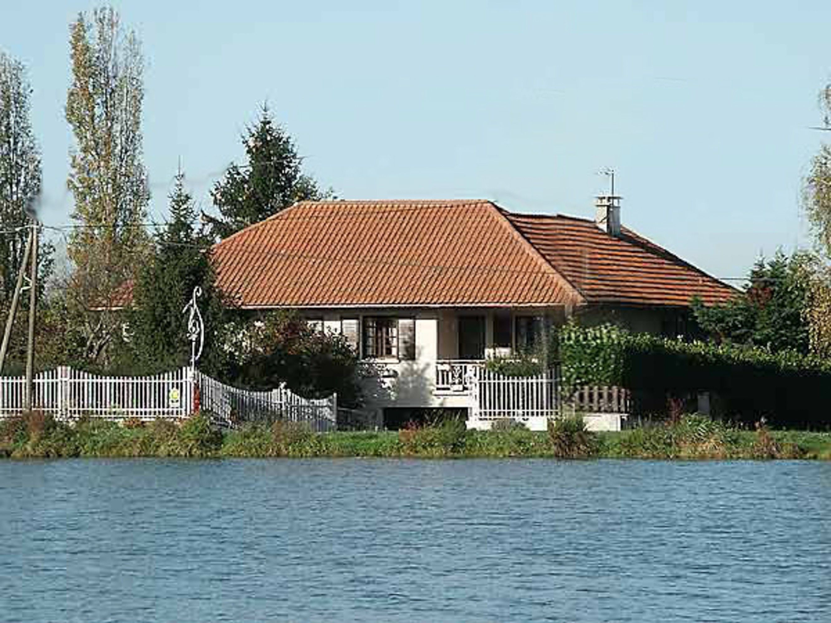 Une maison avec un toit rouge, des murs blancs et une clôture blanche à l’avant.