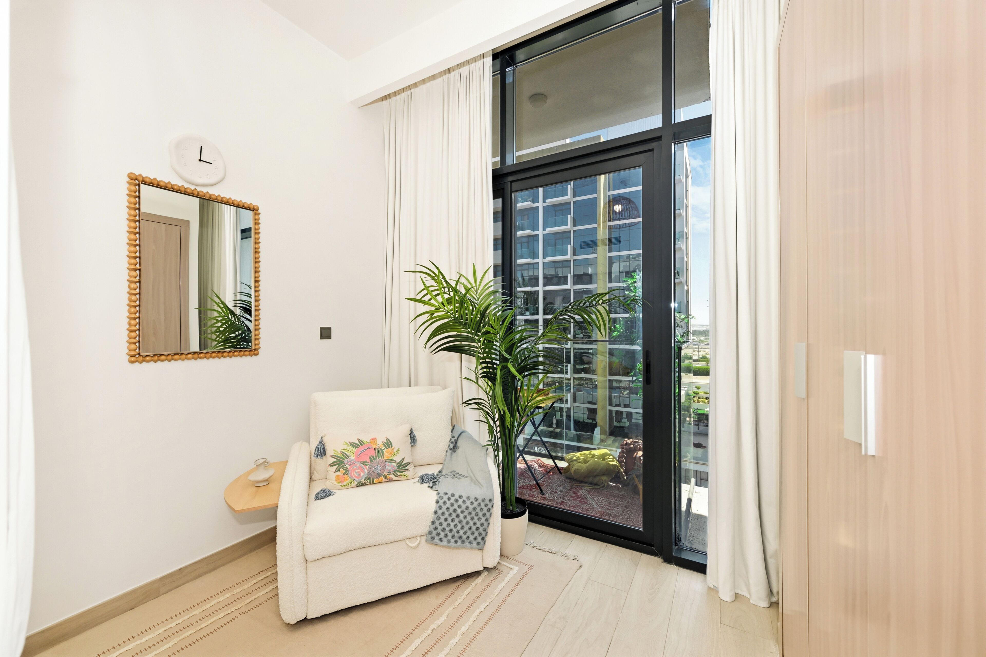 A modern living room with a sofa, a potted plant, a mirror, and a sliding glass door leading to an outdoor area.