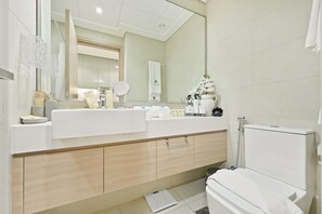 A modern bathroom with a large mirror, two sinks, a toilet, and a shower area. - Bloomfields Studio - Azizi Riviera 35  (Dubai)