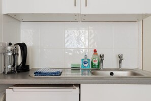A kitchen with white cabinets, a stainless steel sink, a coffee maker, and cleaning supplies. - Cozy Studio Escape by Clapham Common (Greater London)