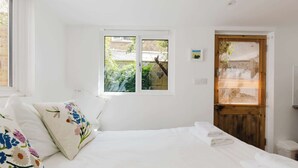 A bedroom with a bed, a window, a door, and a small wall-mounted light. - Cozy Studio Escape by Clapham Common (Greater London)