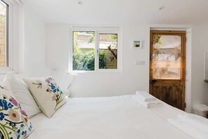 Ein Schlafzimmer mit einem Bett, einem Fenster, einer Tür und einer kleinen Wandleuchte.