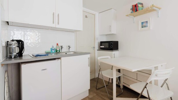 A compact kitchenette with a coffee maker, microwave, and a small shelf with books. - Cozy Studio Escape by Clapham Common (Greater London)