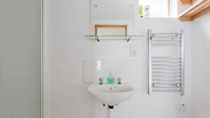 A bathroom with a white sink, a glass shelf above it, and a towel rack to the right. - Cozy Studio Escape by Clapham Common (Greater London)