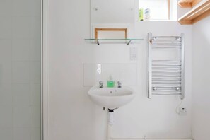Ein Badezimmer mit einem weißen Waschbecken, einer Glasablage darüber und einem Handtuchhalter zur Rechten.
