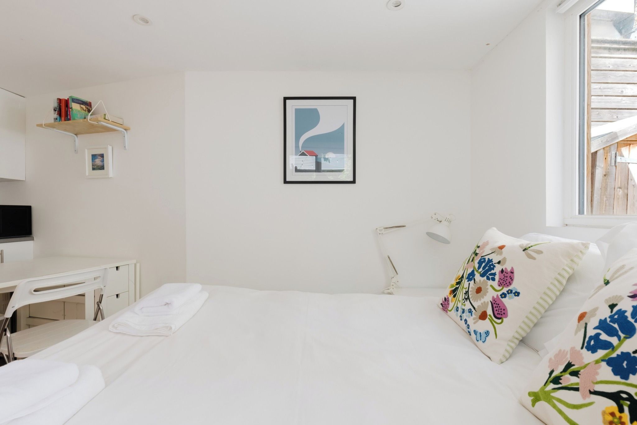 A hotel room with a bed, a desk, a chair, a bedside table, a lamp, and a window.