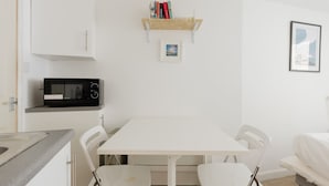 A small, clean room with a white table, two chairs, a microwave, a shelf with books, and a framed picture on the wall. - Cozy Studio Escape by Clapham Common (Greater London)