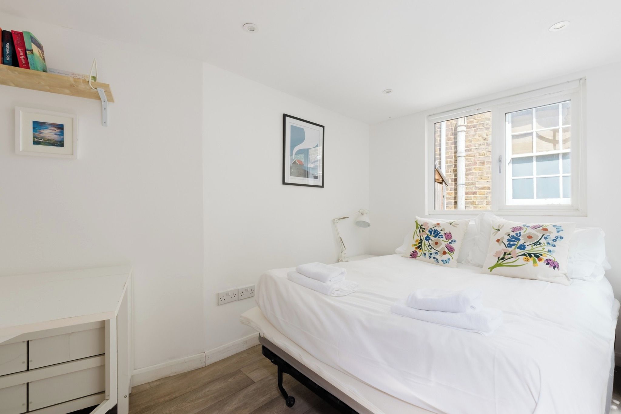 A bedroom with a bed, a bedside table, a window, and a wall-mounted picture.