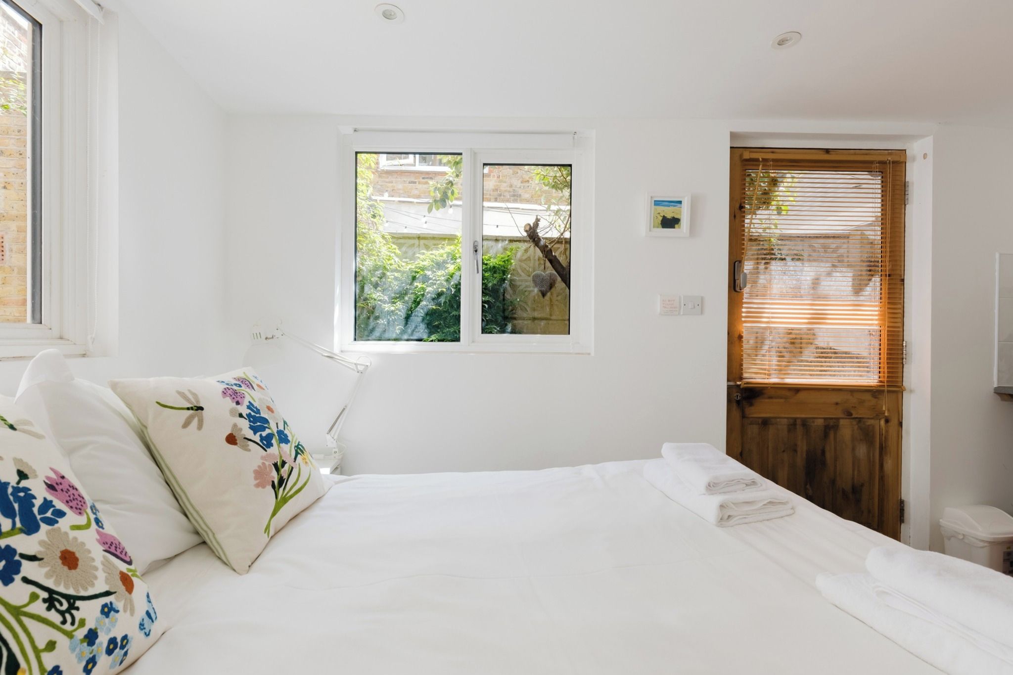 Une chambre à coucher avec un lit, une fenêtre, une porte et une petite lampe fixée au mur.