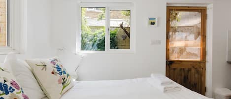 A bedroom with a bed, a window, a door, and a small wall-mounted light.