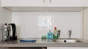 A kitchen with white cabinets, a stainless steel sink, a coffee maker, and cleaning supplies. - Cozy Studio Escape by Clapham Common (Greater London)