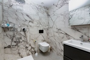 Ein Badezimmer mit Marmorwand, Toilette, Dusche, Waschbecken und Spiegel.