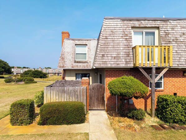 A two-story house with a wooden deck, a brick facade, and a small front yard with trimmed bushes. - Kitty Hawk Family Oasis Pool & Tennis - 1 Mi to Beach (Kitty Hawk)