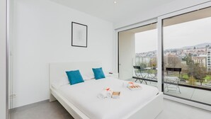 Ein modernes Schlafzimmer mit einem großen Bett, Stadtblick und einem Balkon mit Gartenmöbeln.
