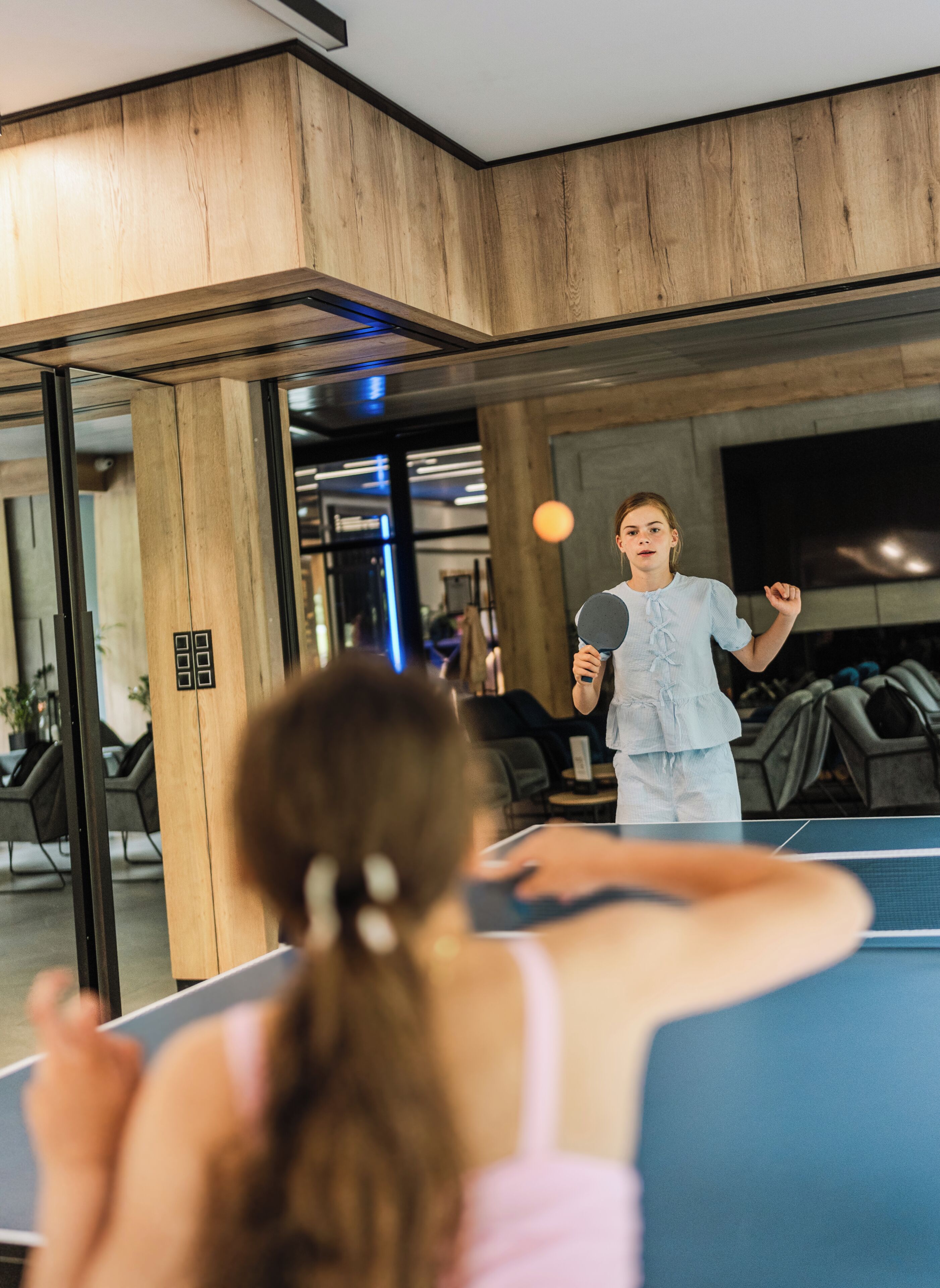 Una mesa de ping pong en una habitación con paredes de madera y un espejo grande.
