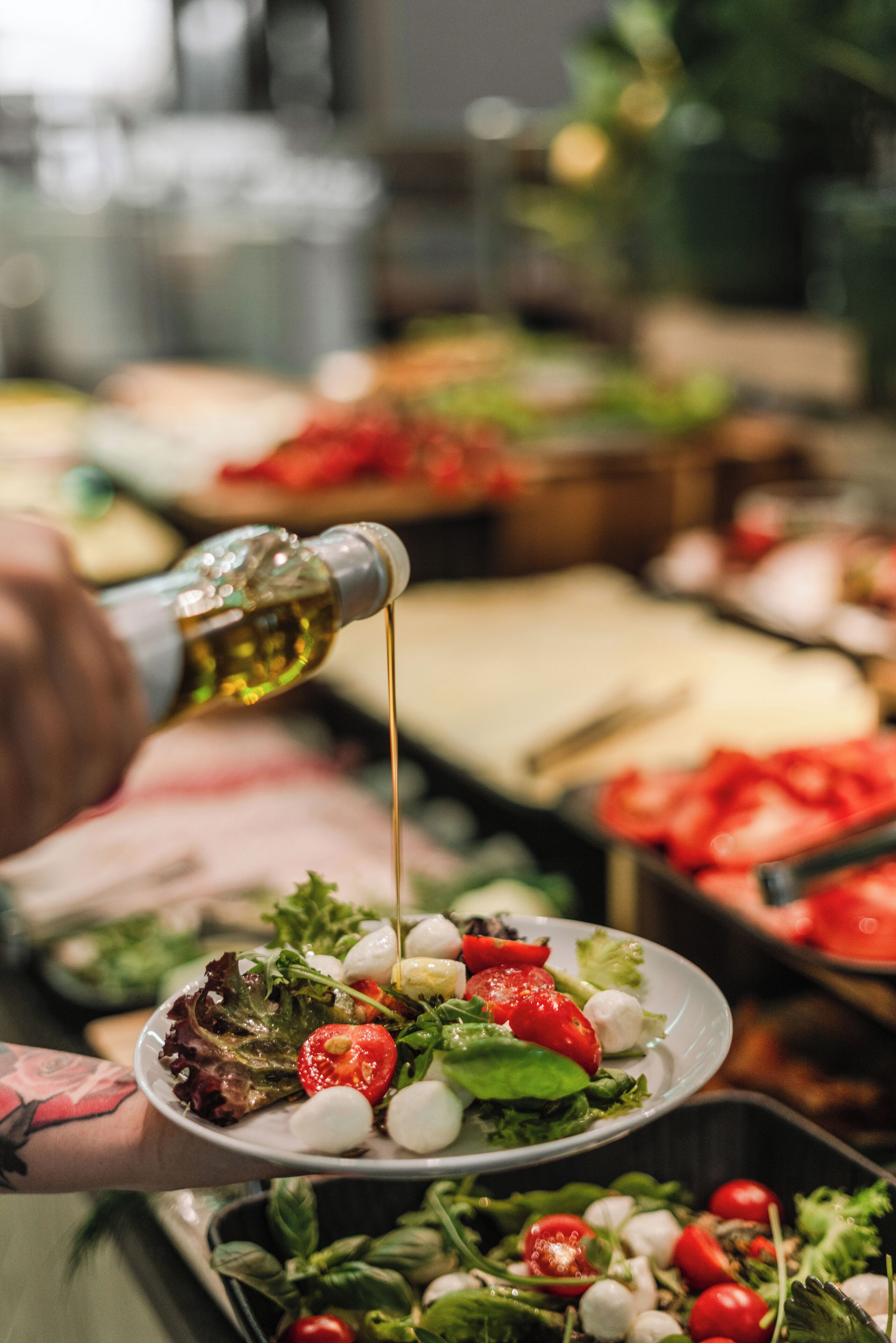 A person pouring olive oil over a salad with tomatoes and mozzarella.