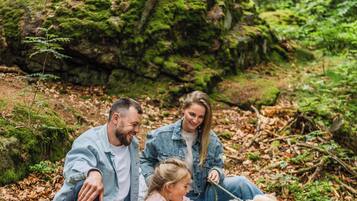 Una famiglia fa un picnic in una foresta, con una roccia ricoperta di muschio, una tovaglia da picnic e un cesto pieno di cibo.
