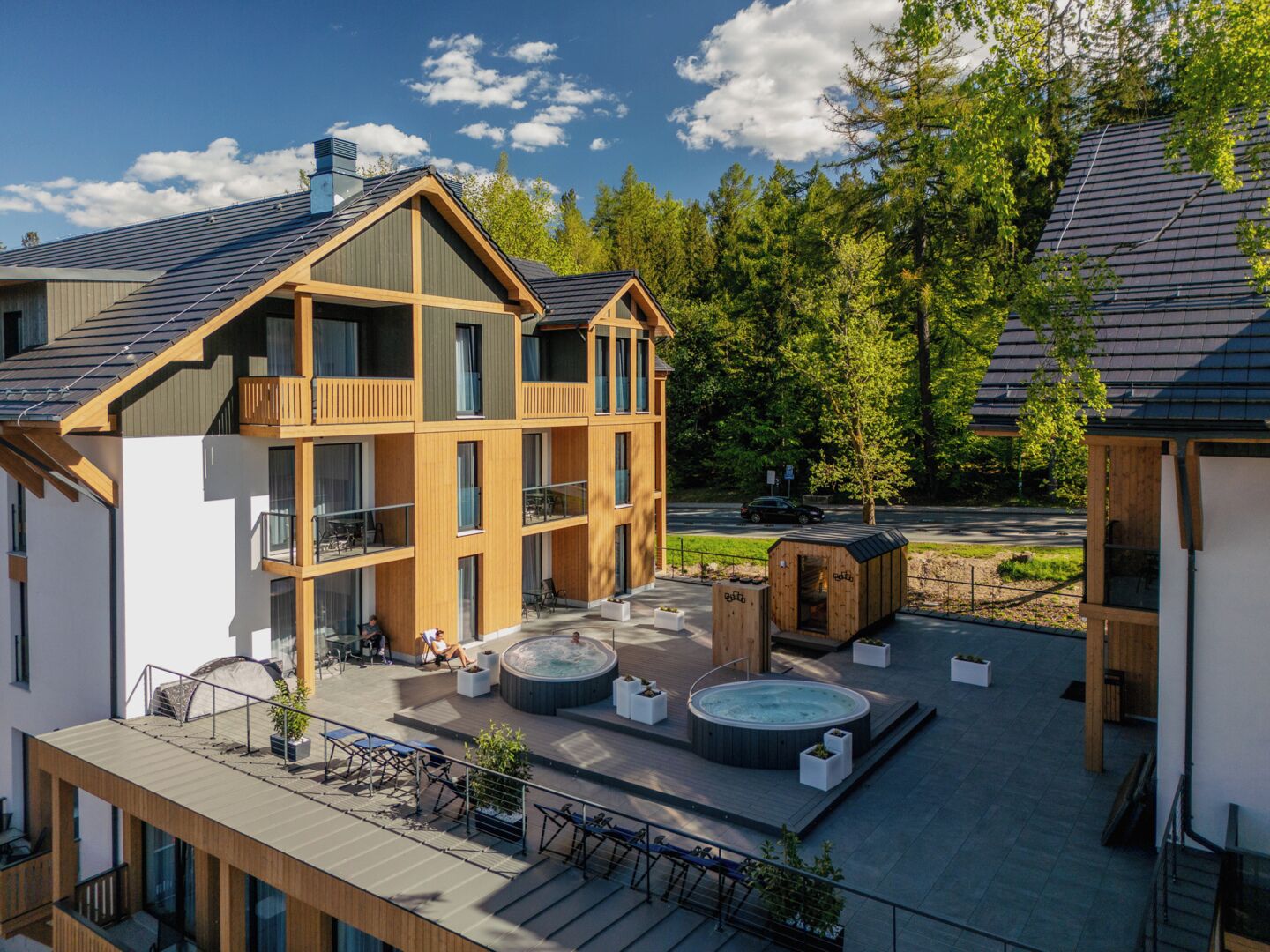 A multi-story building with a rooftop terrace, hot tubs, and a wooden deck.