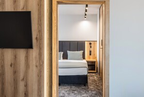 Een hotelkamer met een houten wand, een bed met een grijze hoofdeinde, een nachtkastje en een aan de muur bevestigde televisie.