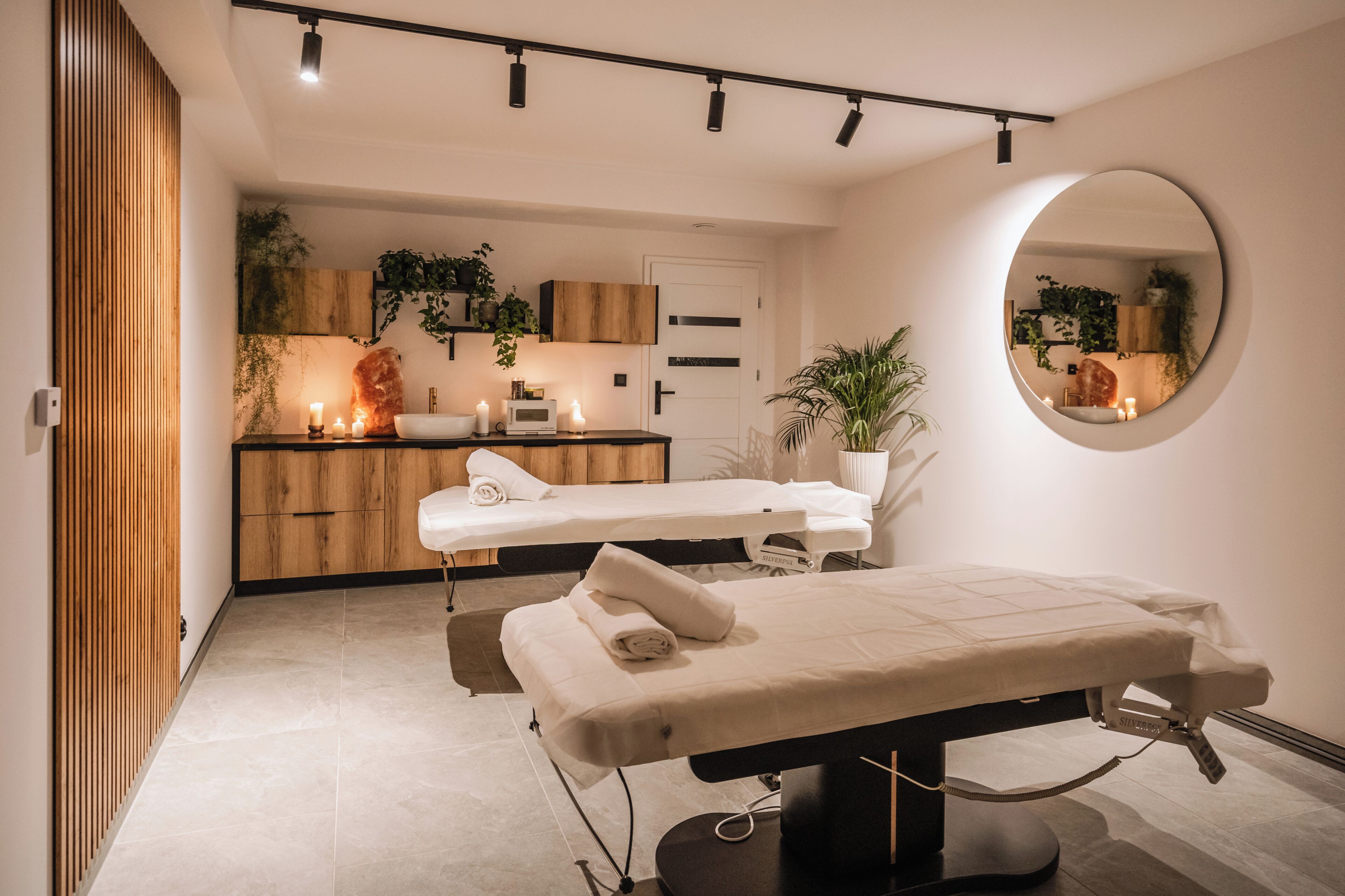 A modern spa room with a massage table, wooden cabinets, and a mirror.
