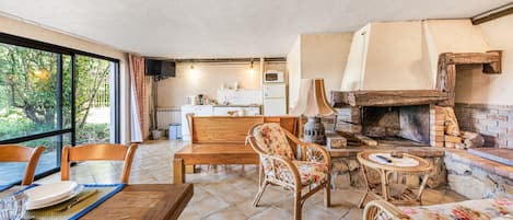 A cozy living area with a wooden table, chairs, a fireplace, and a kitchen in the background.