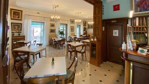 Um saguão de hotel com várias mesas de jantar, cadeiras, lustres e um balcão de recepção.