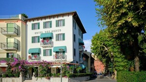 Um hotel com vários andares, varandas, uma placa com a inscrição 'HOTEL SAN MARCO' e uma rua de paralelepípedos.